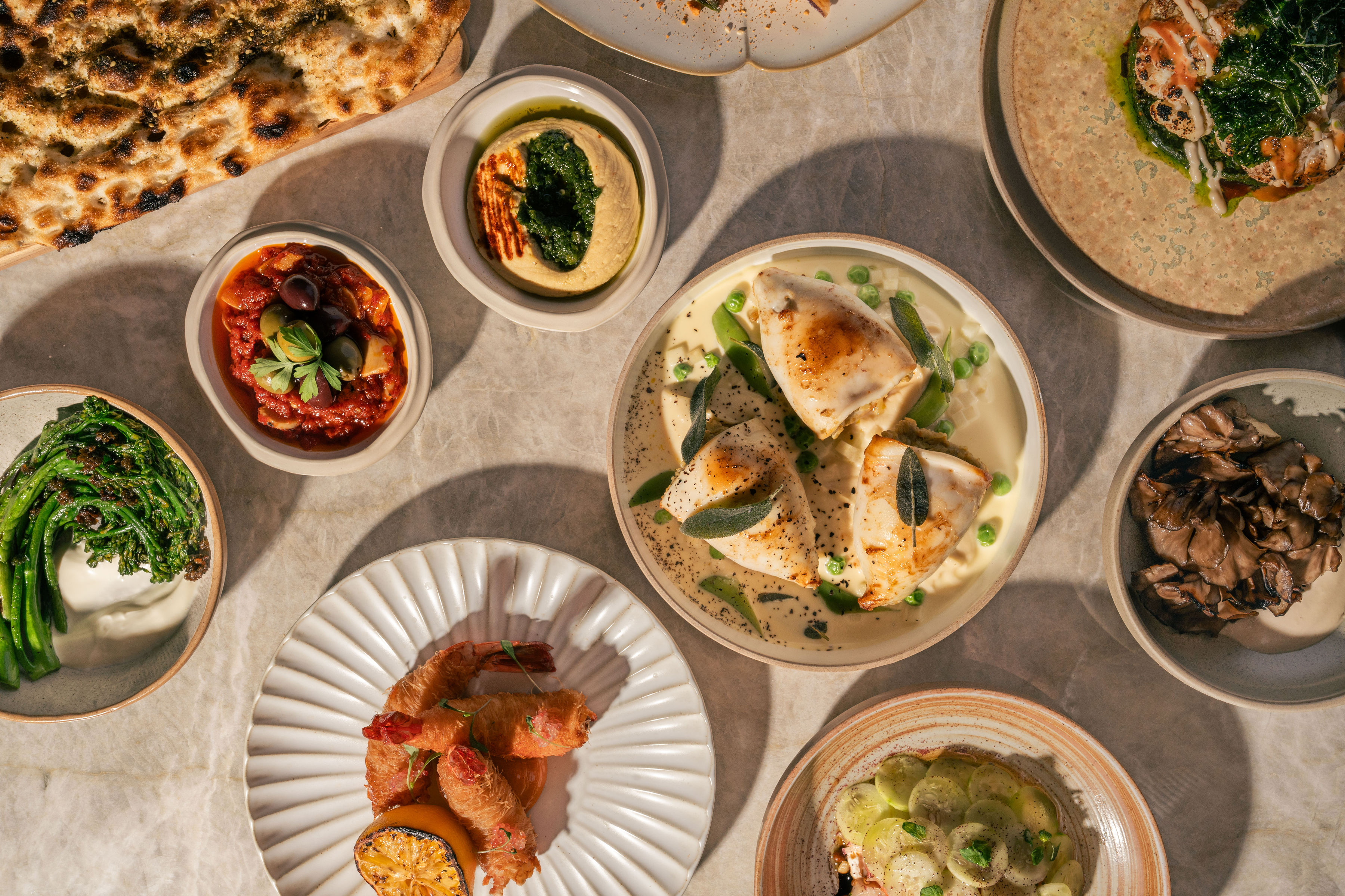 Overhead spread of Petra dishes including flatbread, mezze, seafood and grilled vegetables